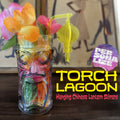 Decorative glass with flowers and a Chinese Lantern "Torch Lagoon" Personalized Swizzle Stick hanging over the edge on a wooden surface, with 'Personalize' branding.