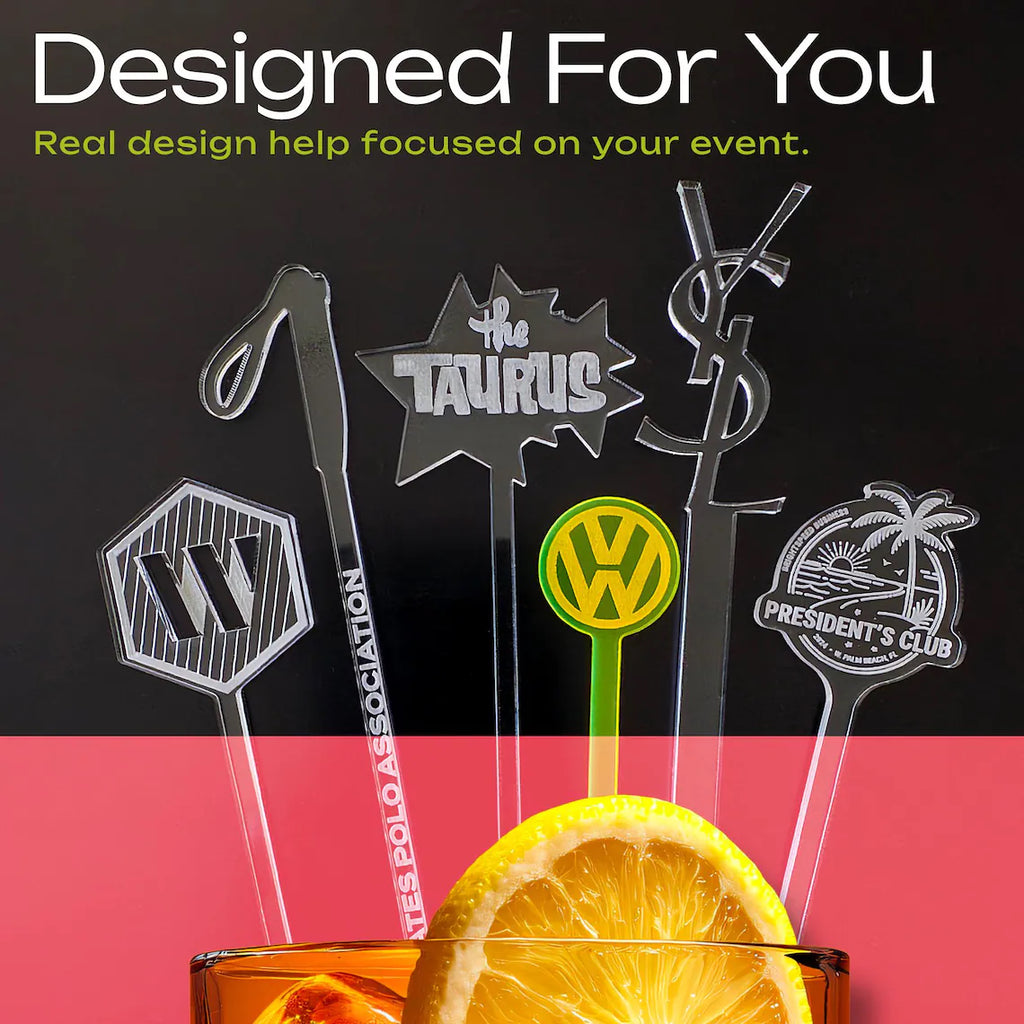 Decorative cocktail drink stirrers with various designs and text, placed in a glass with a lemon slice on a black and red background.