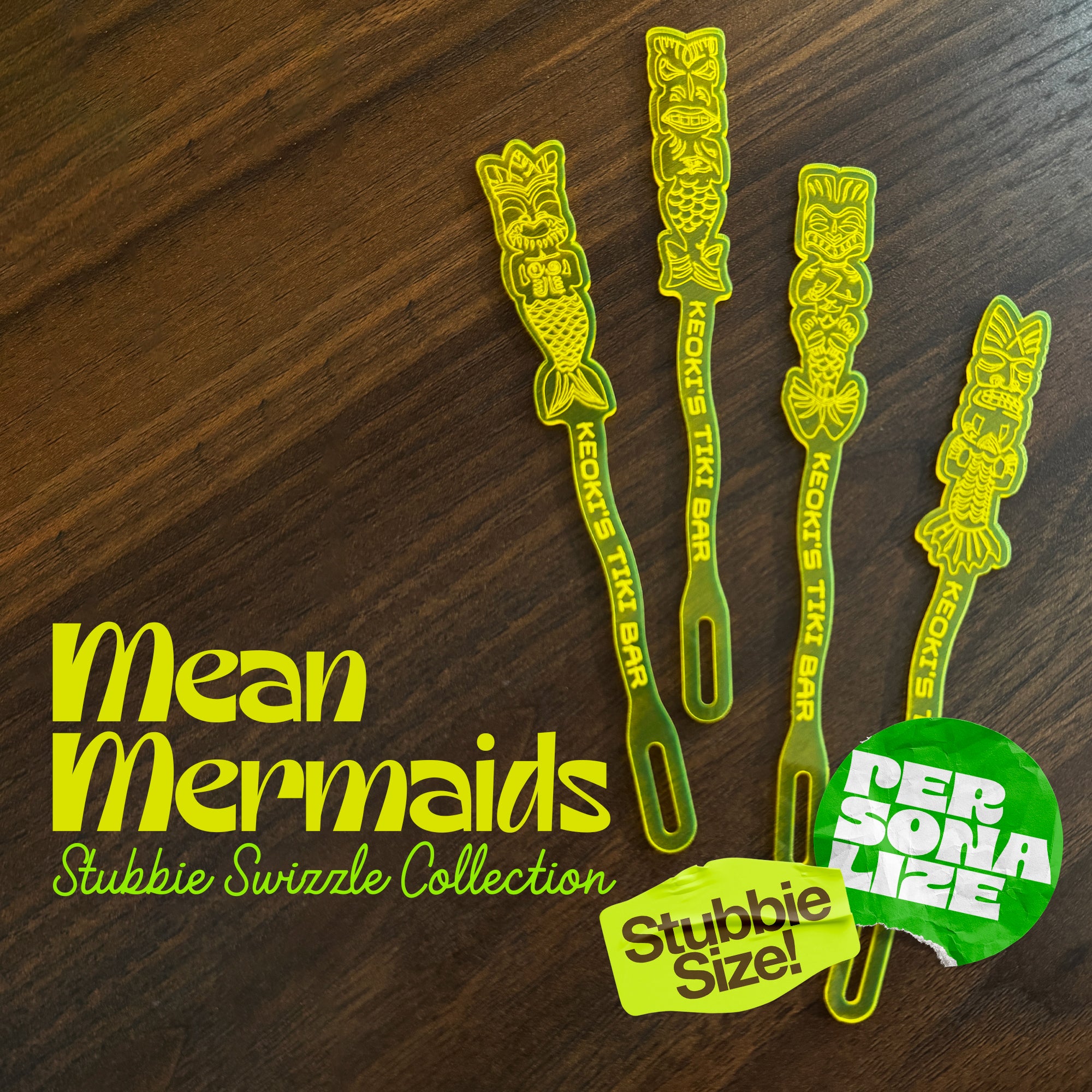 Mean Mermaids Personalized Stubbie Swizzle Sticks arranged on a dark wood surface, with large white text and two colorful promotional badges.