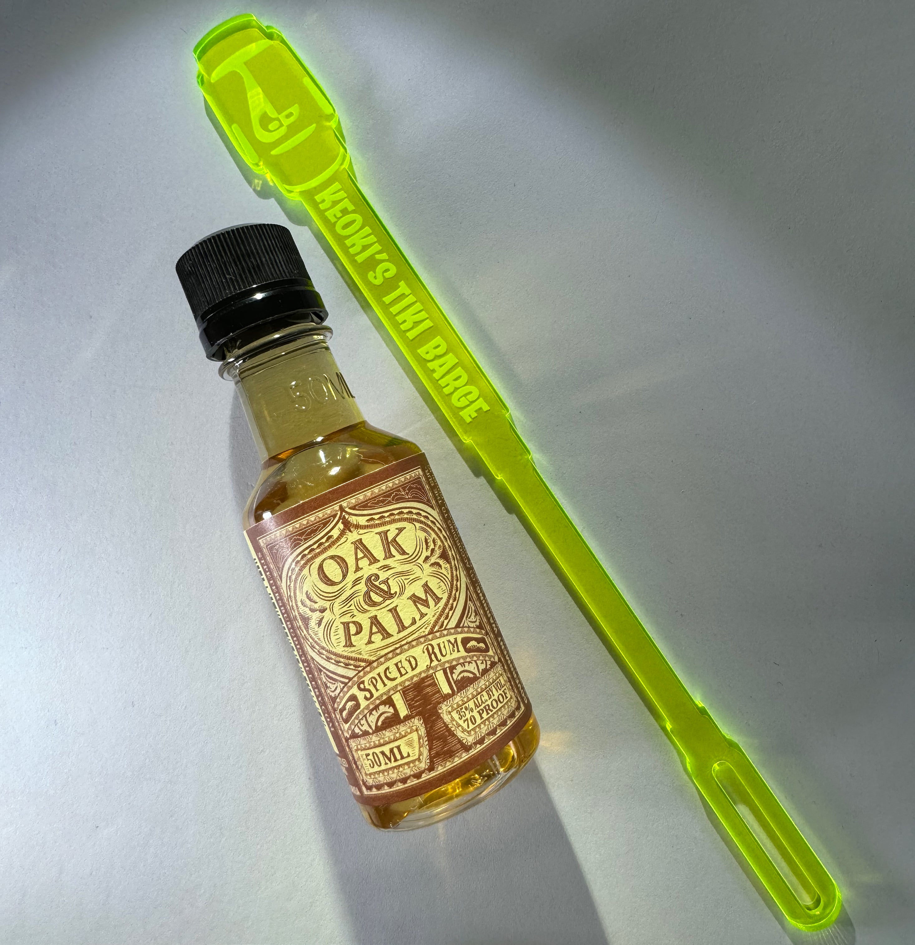 Small bottle of 'Oak & Palm Spiced Rum' with a Moai Statue Personalized XL Swizzle Stick on a white background