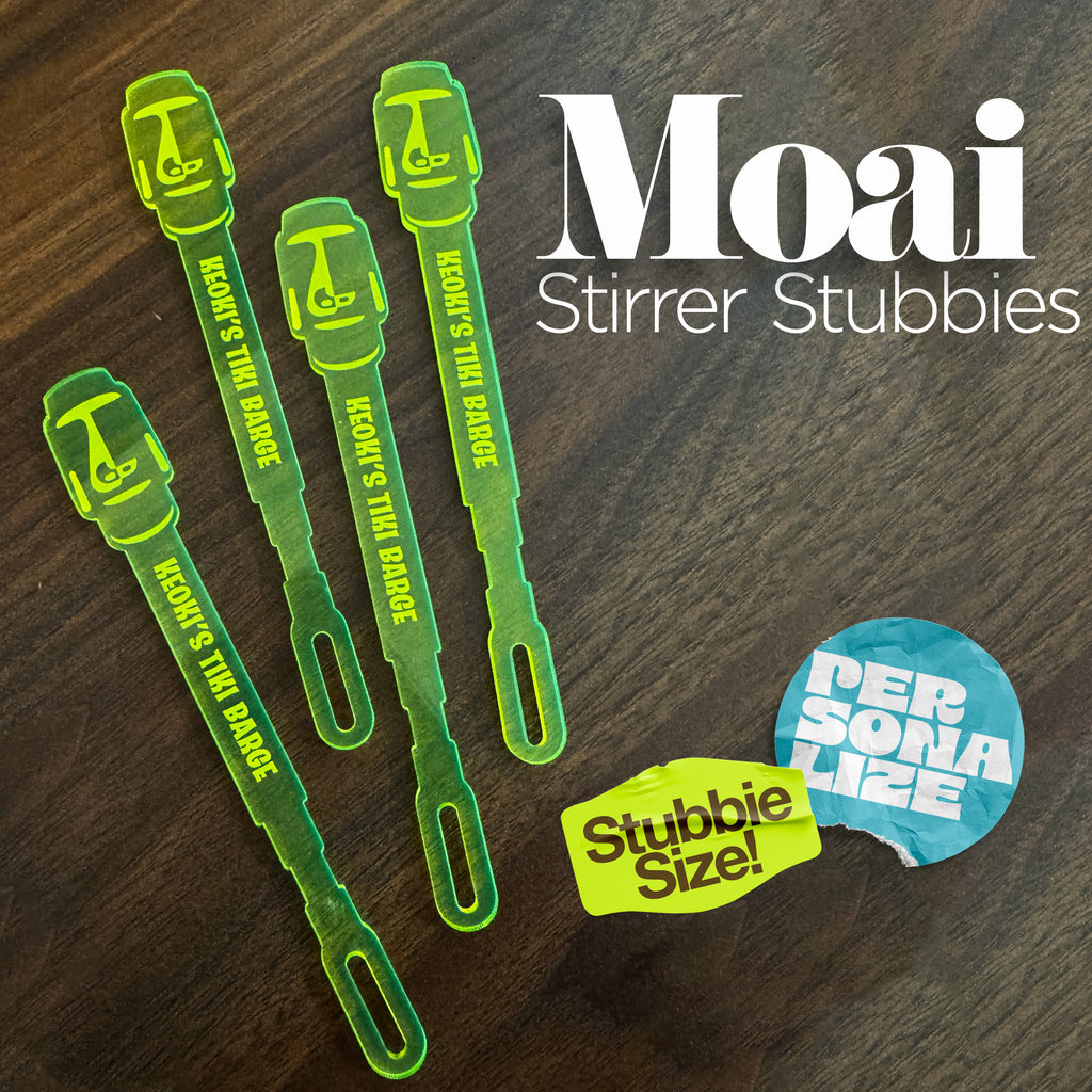 Moai Statue Stubbie Drink Stirrers on a dark wood background, with large white text reading 'Moai Stirrer Stubbies' and two colorful promotional stickers.
