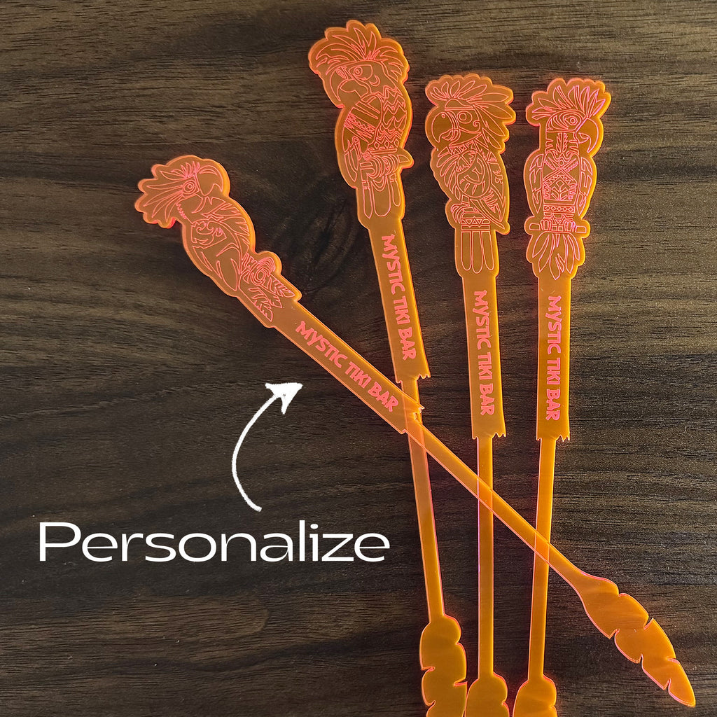 Four orange Parrot cocktail drink stirrers with floral designs on a wooden surface, branded 'Mystic Thai Bar'.
