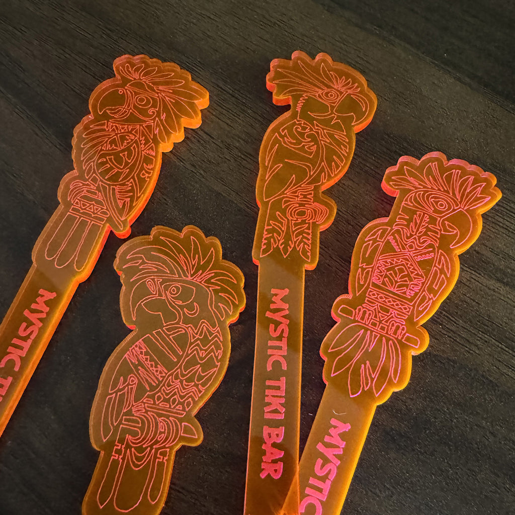 Four translucent Parrot cocktail drink stirrers with tiki design and 'Mystic Tiki Bar' text on a dark surface.