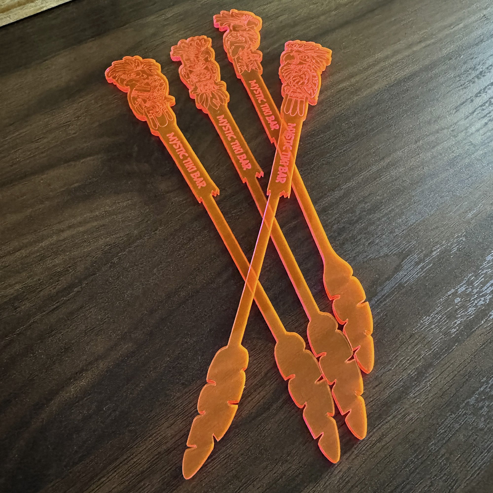 Set of orange Parrot drink stirrers with decorative leaf ends on a wooden surface