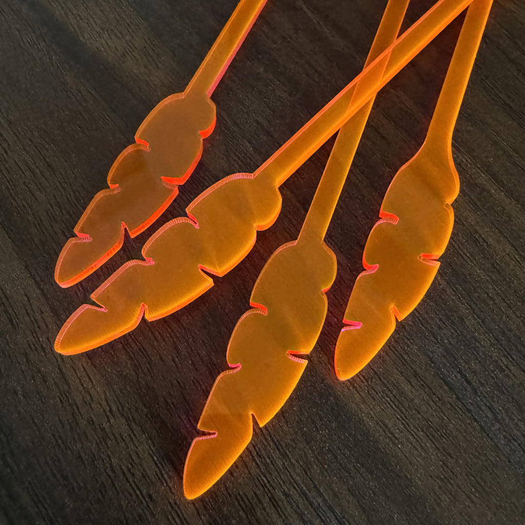 Orange banana leaf shaped end of a Parrot swizzle stick on a dark wooden surface