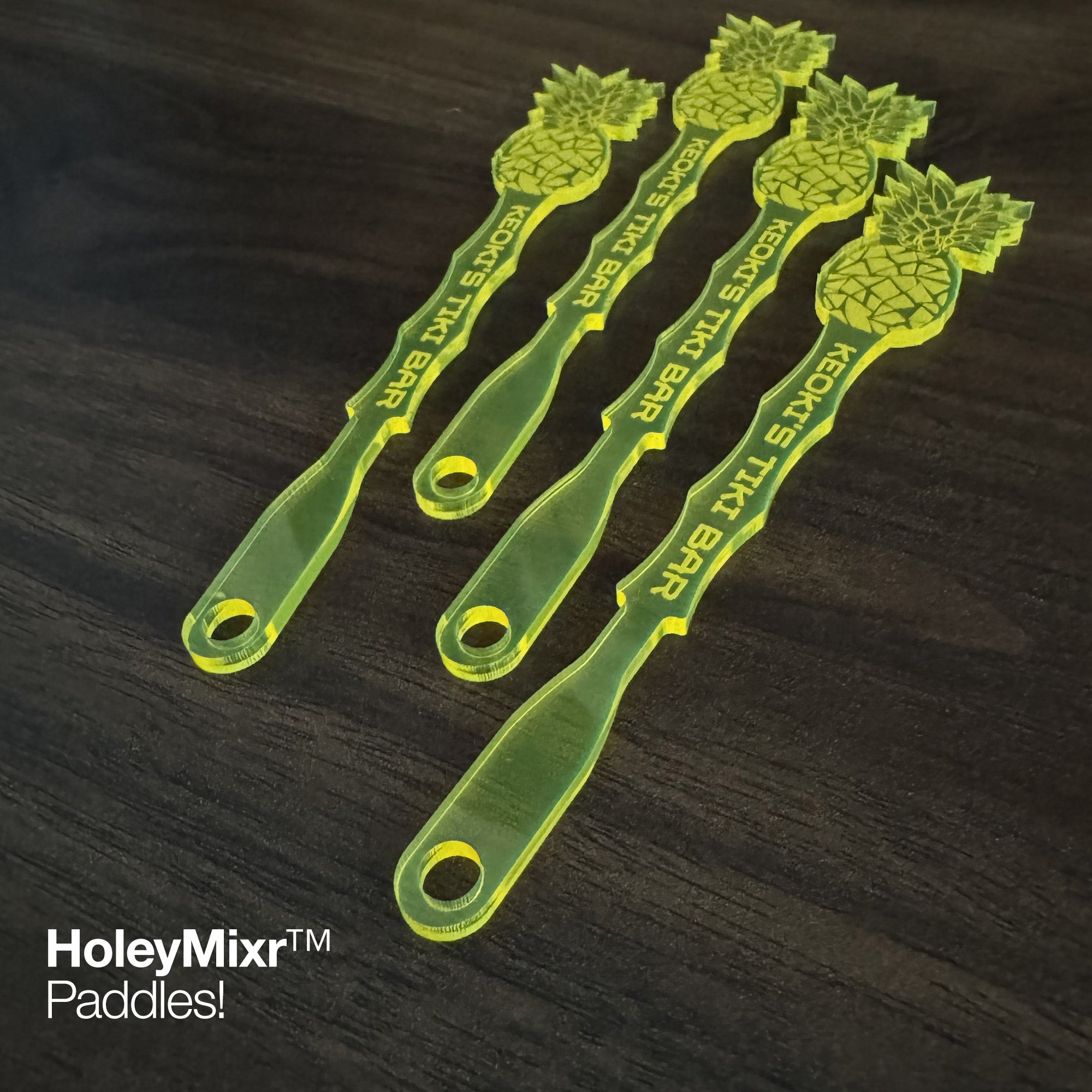 Four Pineapple personalized drink stirrrers on a dark wooden surface with brand name visible.