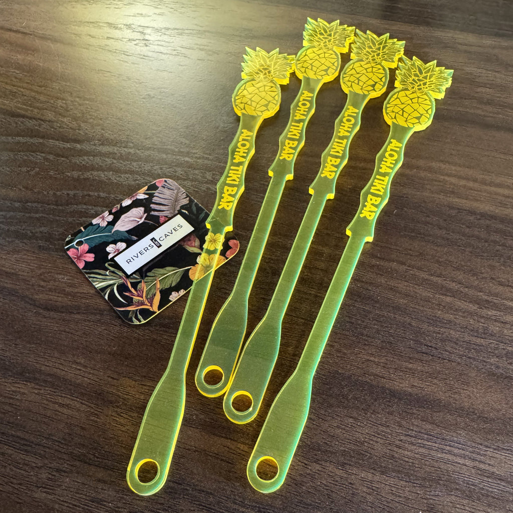 Pineapple shaped personalized drink stirrers on a wooden surface with a floral card in the background.