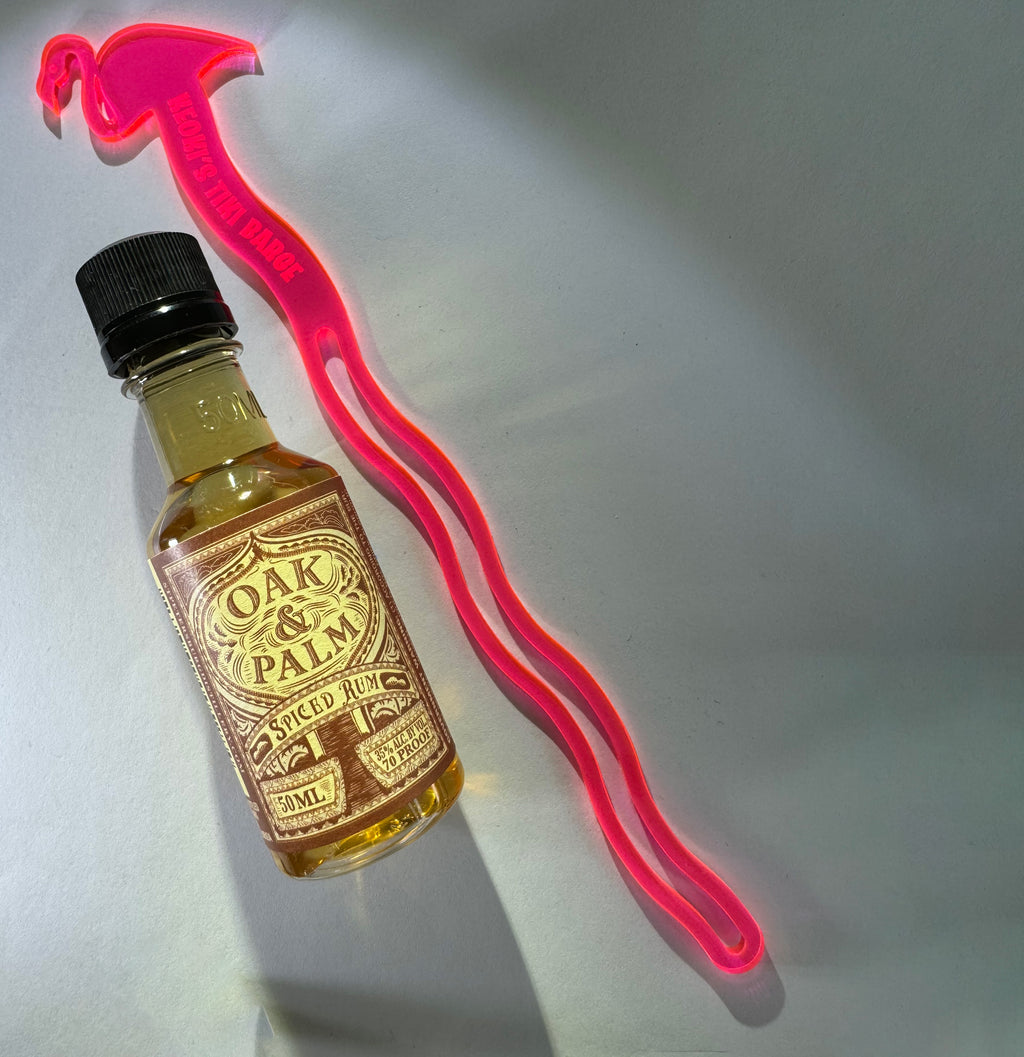 Small bottle of Oak & Palm rum with a Pink Flamingo Personalized Drink Stirrer on a gray background