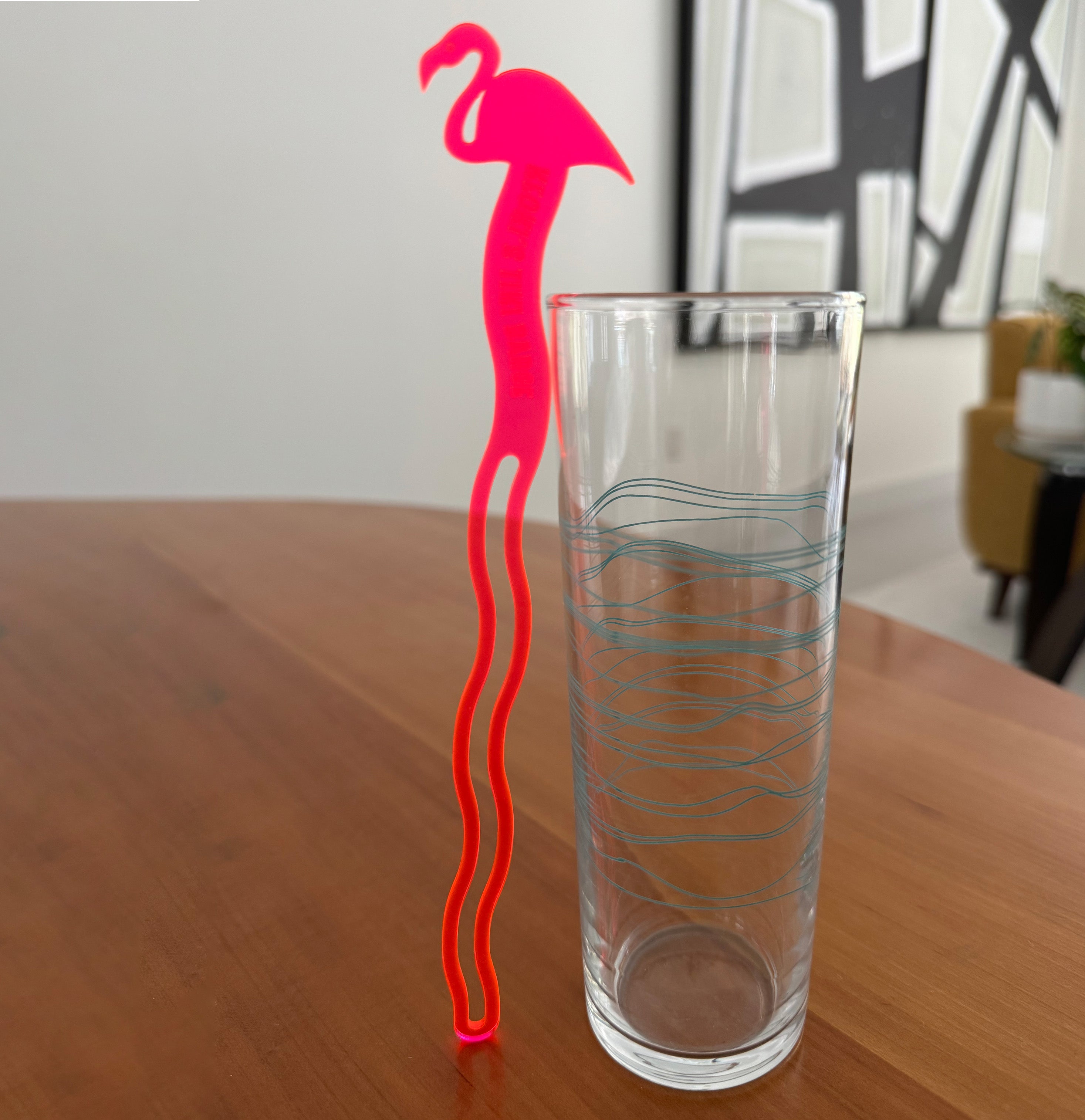 Clear glass with a Pink Flamingo Personalized Drink Stirrer on a wooden surface.