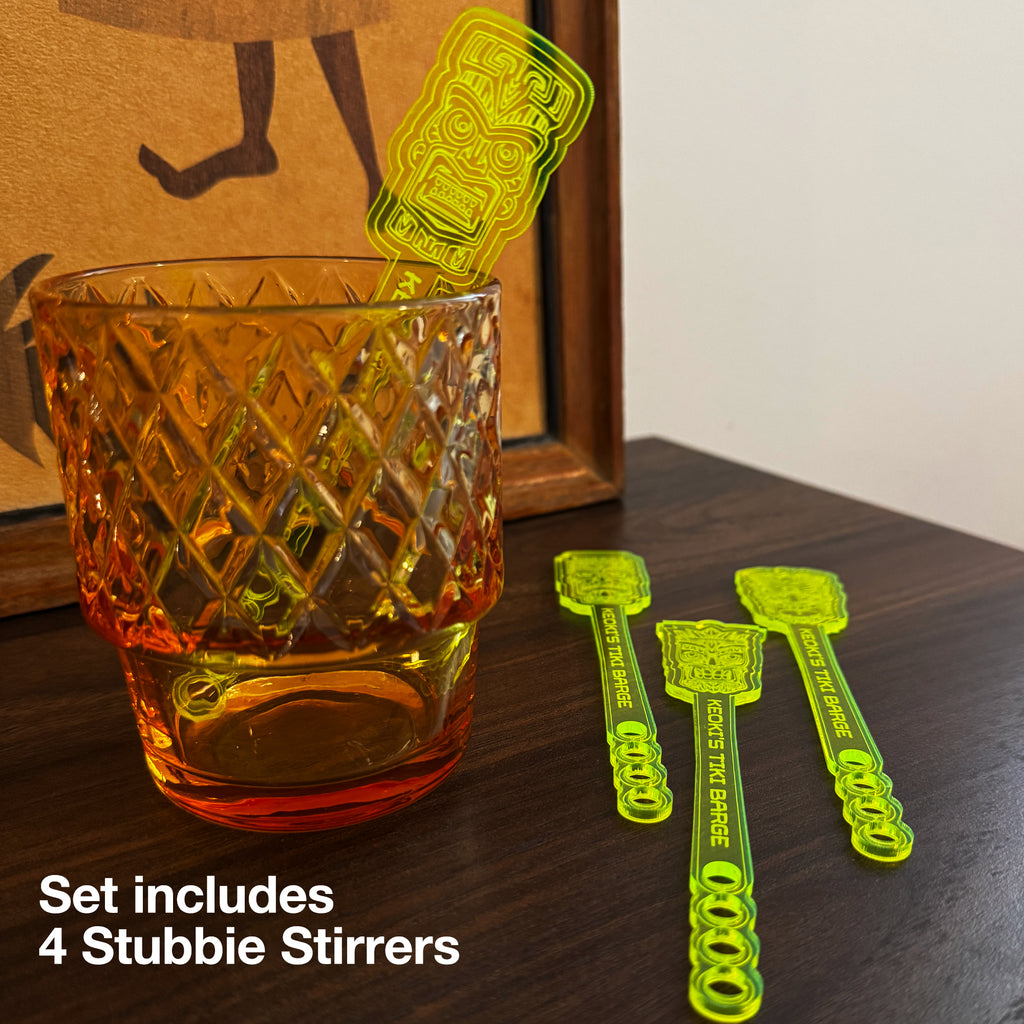 A textured amber glass tumbler on a wooden surface next to a Tiki Neue Stubbie Drink Stirrer . White text overlay says 'Set includes 4 Stubbie Stirrers'.