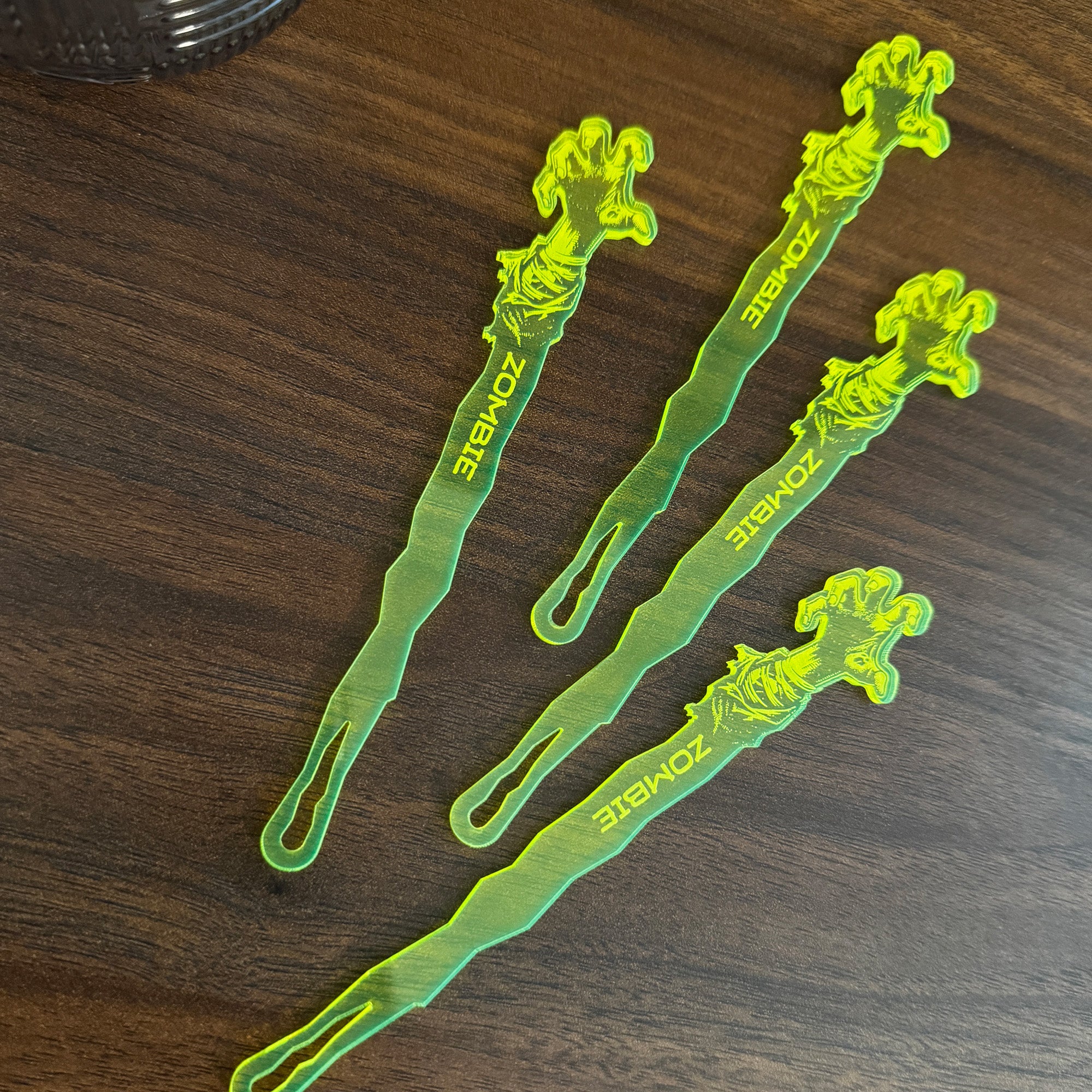 Zombie Personalized Stubbie Swizzle Sticks resting on a dark wooden table next to an glass tumbler.